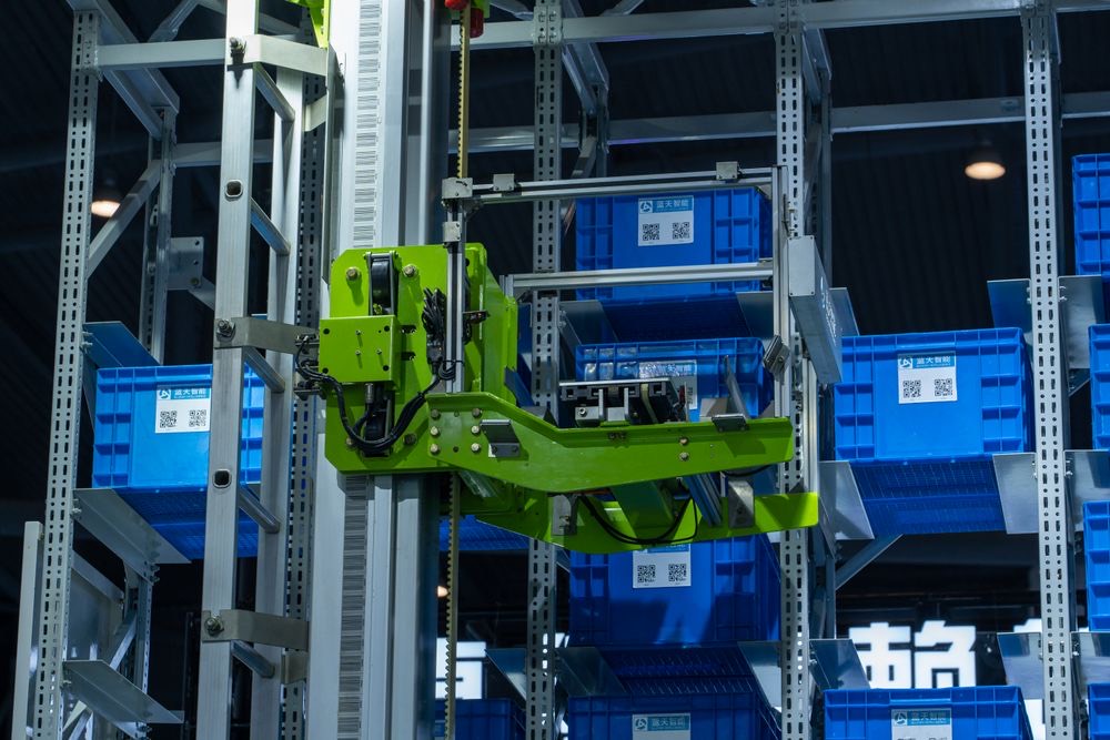 A robotic picker lifting a blue storage crate from racking in an automated warehouse.