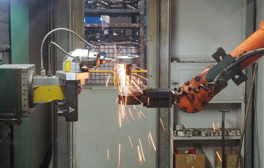 An industrial robot arm welding a steel part, throwing sparks.